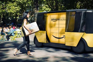 A girl with a package is walking up to the self driving vehicle which is an amazon locker