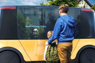 Father and son are standing in front of a driverless school bus who's window reads Good morning, Finley